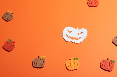 Turuncu arka planda beyaz kağıt balkabağı. Fotokopi alanı ve çeşitli sonbahar renklerinde keçeli dekoratif diğerleri. Metin veya logo eklemek için sol yüzey boş