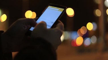 Bir kişi manifatura onun smartphone cep telefonu ile gece portre. Güzel bokeh arka plandan sokak ışıkları.