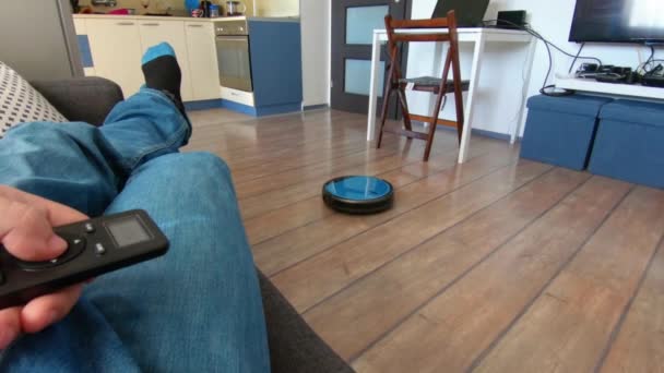 Persona que se relaja en un sofá con robot de vacío remoto en la mano — Vídeos de Stock