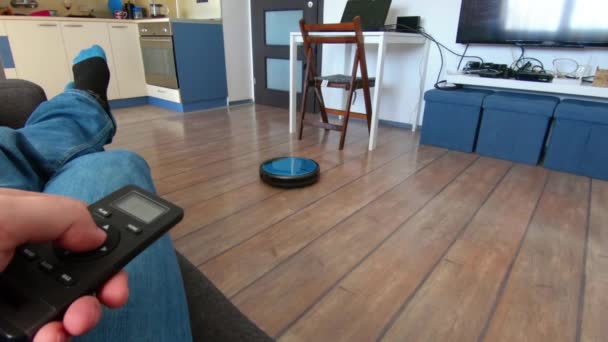 Person som kopplar av på en soffa med robot vacuum fjärrkontroll i hand — Stockvideo