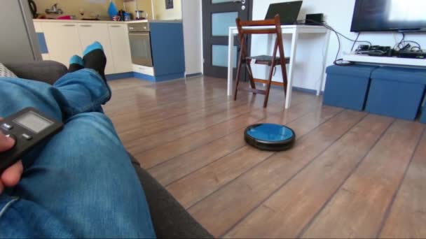 Person som kopplar av på en soffa med robot vacuum fjärrkontroll i hand — Stockvideo