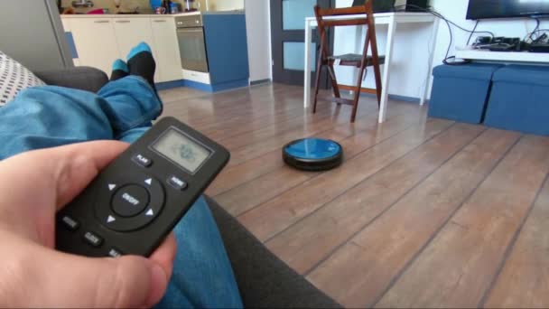 Person som kopplar av på en soffa med robot vacuum fjärrkontroll i hand — Stockvideo