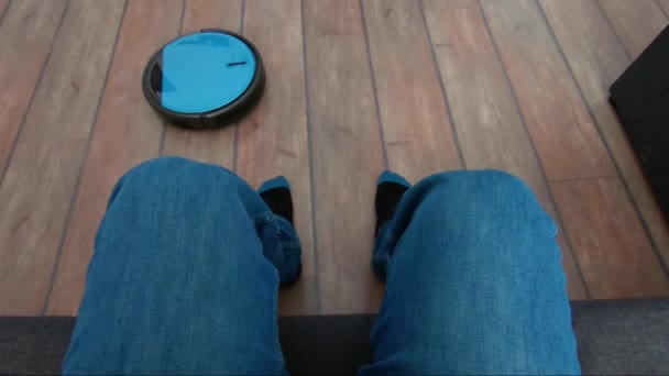 Person som kopplar av på en soffa med robot vacuum fjärrkontroll i hand — Stockvideo