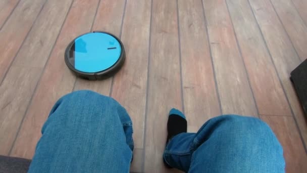 Person relaxing on a sofa with robot vacuum remote in hand — Stock Video
