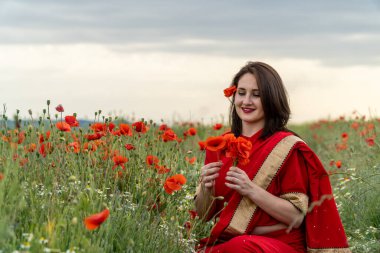 Geleneksel Hint kostümü giymiş genç bir kadın. Adı Sari. Kırmızı gelincik tarlasında yürüyor.