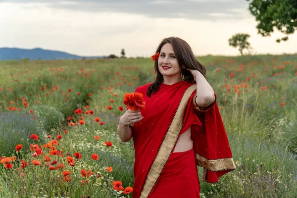 Geleneksel Hint kostümü giymiş genç bir kadın. Adı Sari. Kırmızı gelincik tarlasında yürüyor.