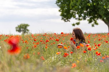 Haşhaş tarlasında mavi elbiseli genç bir kadın. Arkasında güzel bulutlar var.