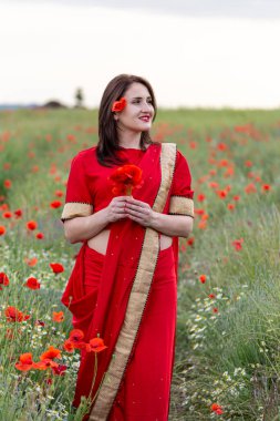 Geleneksel Hint kostümü giymiş genç bir kadın. Adı Sari. Kırmızı gelincik tarlasında yürüyor.