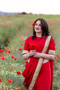 Geleneksel Hint kostümü giymiş genç bir kadın. Adı Sari. Kırmızı gelincik tarlasında yürüyor.