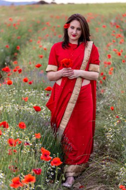 Geleneksel Hint kostümü giymiş genç bir kadın. Adı Sari. Kırmızı gelincik tarlasında yürüyor.