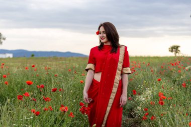 Geleneksel Hint kostümü giymiş genç bir kadın. Adı Sari. Kırmızı gelincik tarlasında yürüyor.