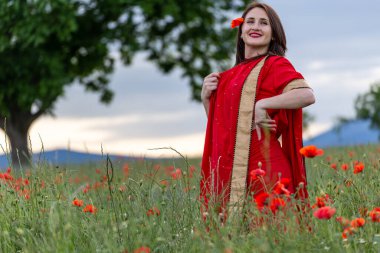 Geleneksel Hint kostümü giymiş genç bir kadın. Adı Sari. Kırmızı gelincik tarlasında yürüyor.