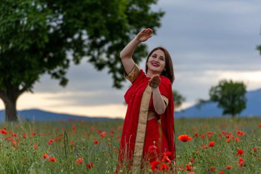 Geleneksel Hint kostümü giymiş genç bir kadın. Adı Sari. Kırmızı gelincik tarlasında yürüyor.