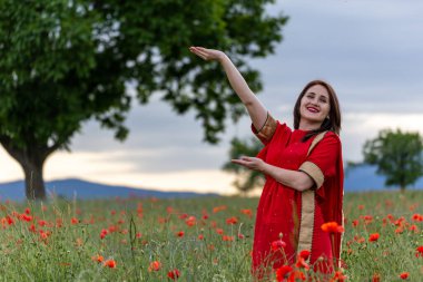 Geleneksel Hint kostümü giymiş genç bir kadın. Adı Sari. Kırmızı gelincik tarlasında yürüyor.