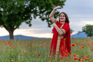 Geleneksel Hint kostümü giymiş genç bir kadın. Adı Sari. Kırmızı gelincik tarlasında yürüyor.