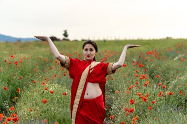 Geleneksel Hint kostümü giymiş genç bir kadın. Adı Sari. Kırmızı gelincik tarlasında yürüyor.