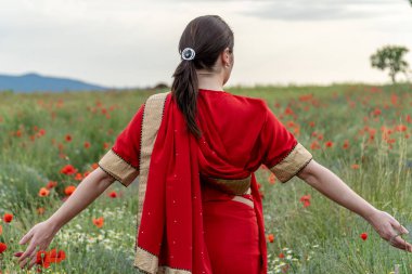 Geleneksel Hint kostümü giymiş genç bir kadın. Adı Sari. Kırmızı gelincik tarlasında yürüyor.
