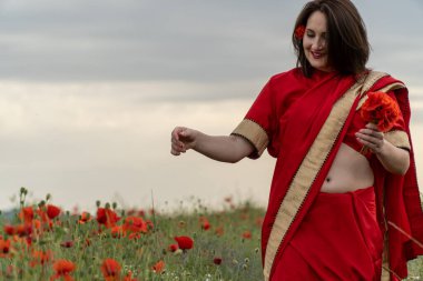 Geleneksel Hint kostümü giymiş genç bir kadın. Adı Sari. Kırmızı gelincik tarlasında yürüyor.