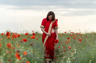 Geleneksel Hint kostümü giymiş genç bir kadın. Adı Sari. Kırmızı gelincik tarlasında yürüyor.