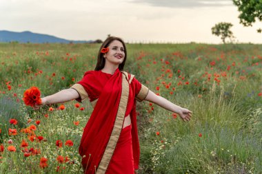 Geleneksel Hint kostümü giymiş genç bir kadın. Adı Sari. Kırmızı gelincik tarlasında yürüyor.