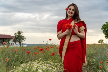 Geleneksel Hint kostümü giymiş genç bir kadın. Adı Sari. Kırmızı gelincik tarlasında yürüyor.