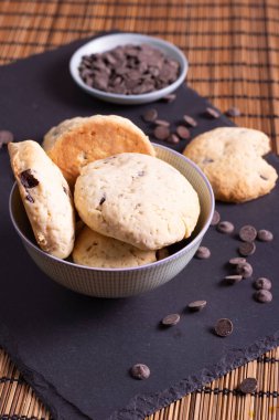 Çikolata parçalı kurabiye kasesi çikolatalı ve bir ısırık kurabiyesi bambu arka planda servis ediliyor.