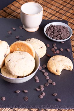 Çikolata parçalı kurabiye kasesi çikolatalı ve bir ısırık kurabiyesi bambu arka planda servis ediliyor.