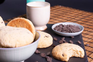 Çikolata parçalı kurabiye kasesi çikolatalı ve bir ısırık kurabiyesi bambu arka planda servis ediliyor.