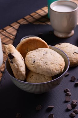Tahtada çikolatalı kurabiye ve bambudan yapılmış bir bardak süt.