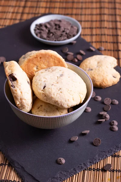 Çikolata parçalı kurabiye kasesi çikolatalı ve bir ısırık kurabiyesi bambu arka planda servis ediliyor.