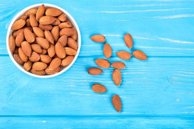 Beyaz seramik kase ile fındık badem tam bir mavi ahşap arka plan üzerinde üstten görünüm dağınık