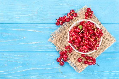 Kase taze kırmızı kuş üzümü çuval bezi ve ahşap zemin, üstten görünüm üzerinde dağınık çilek ile dolu