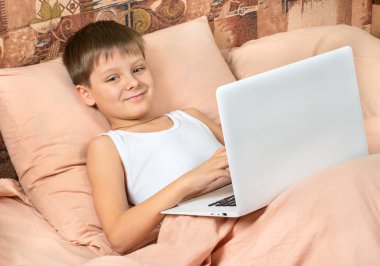Boy gülümseyerek yatakta bir dizüstü bilgisayarda Internet üzerinde iletişim kurar