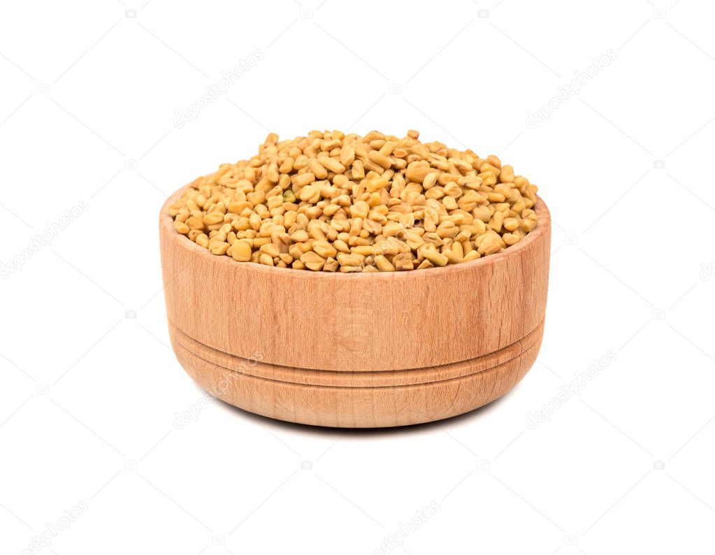 Dry seeds of fenugreek in a wooden bowl isolated on white background
