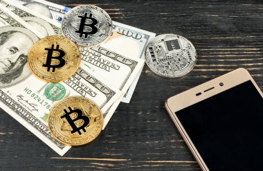 Altın ve gümüş bitcoin paralar ile dolar ve ahşap arka plan üstünde smartphone
