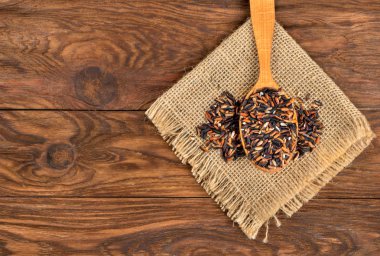 Çuval bezi ve ahşap arka plan kaşık çiğ yabani pirinç