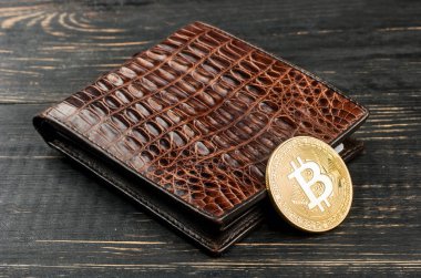 Masanın üzerinde bir altın bitcoin sikke ile deri çanta