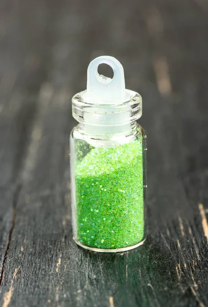 Green glitters for nail design and make-up on wooden background