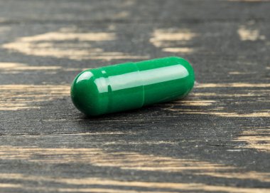 Ahşap arka plan üzerinde yeşil bitkisel kapsül