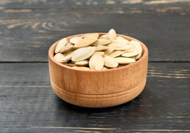 Ahşap arka plan üzerinde kabuğundaki kabak çekirdeği ile küçük kase