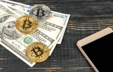 Altın ve gümüş bitcoin paralar ile dolar ve ahşap arka plan üstünde smartphone
