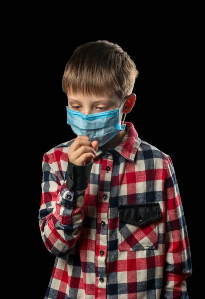 Sick boy in medical mask coughs on black background