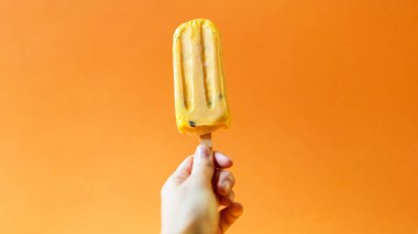 Kızın elini Mango Dondurma parlak bir turuncu arka planda tutan.