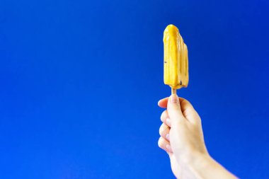 Kızın elini derin mavi bir arka plan üzerinde parlak sarı dondurma.