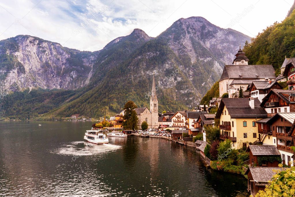Hallstatt town in Austrian alps with cozy old houses and touristic ferry on lake. 