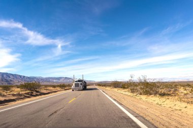 Kamyon sürme, kumlu yol kenarları ve ufukta dağlar ile bir çölde Yol. California, Amerika Birleşik Devletleri.