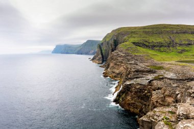 Yamaç kayalıkları ve ufukta yağmur bulutu ile bosdalafossur şelale Panoraması. Vagar, Faroe Adaları.