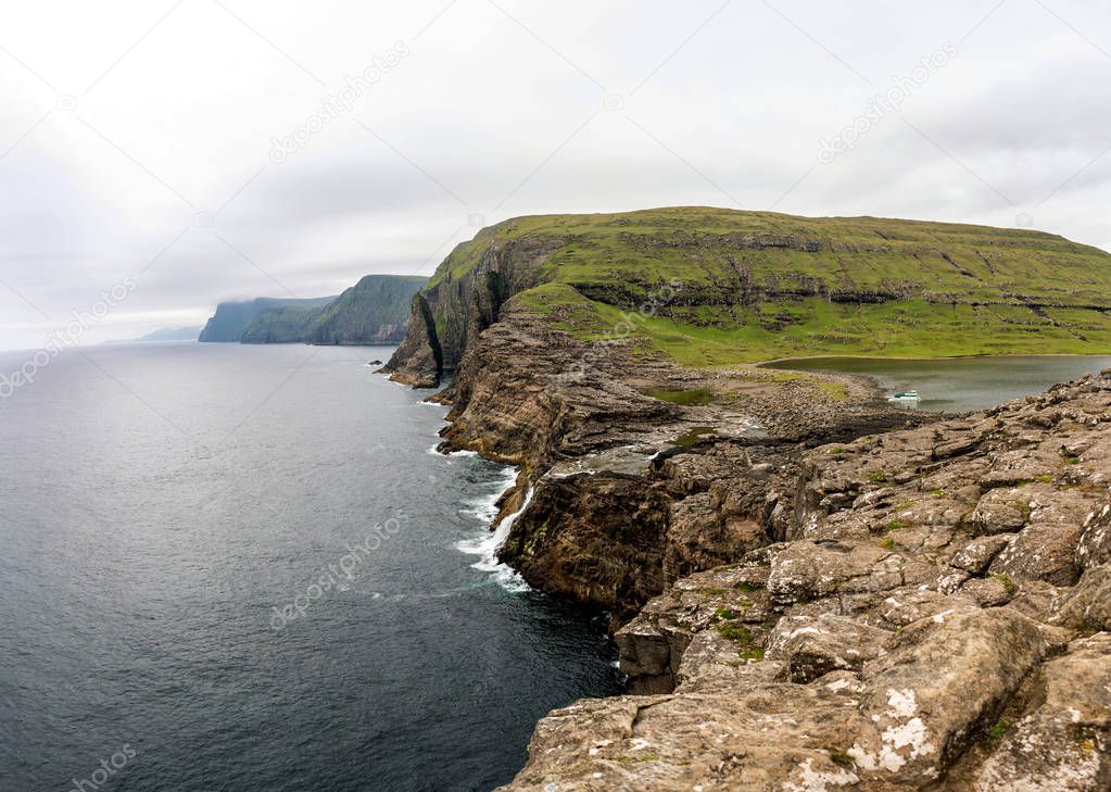Leitisvatn lake flows into the Atlantic ocean and cliff rocks on horizon. Vagar, Faroe Islands.