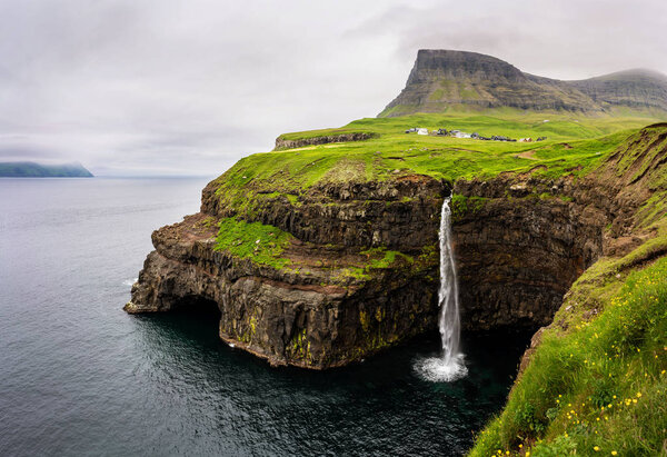 One of the greatest Faroese landmarks - Gasadalur village and Mulafossur waterfall stunning panorama. Vagar, Faroe Islands.
