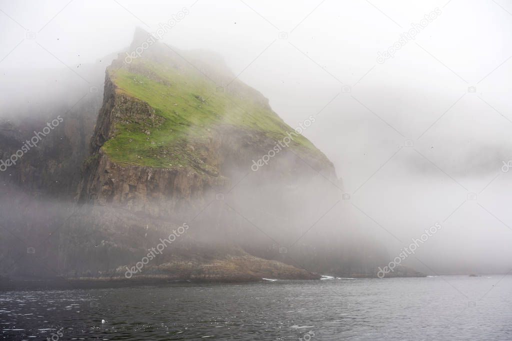 Absolutely stunning Mykines Island shoot from water: Green cliffs and thick fog around. Faroe Islands. 